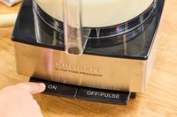 A person presses the 'ON' button on the front of the Cuisinart 14-Cup Food Processor