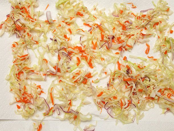 Shredded and salted cabbage, onion, and carrot strewn over paper towels to dry