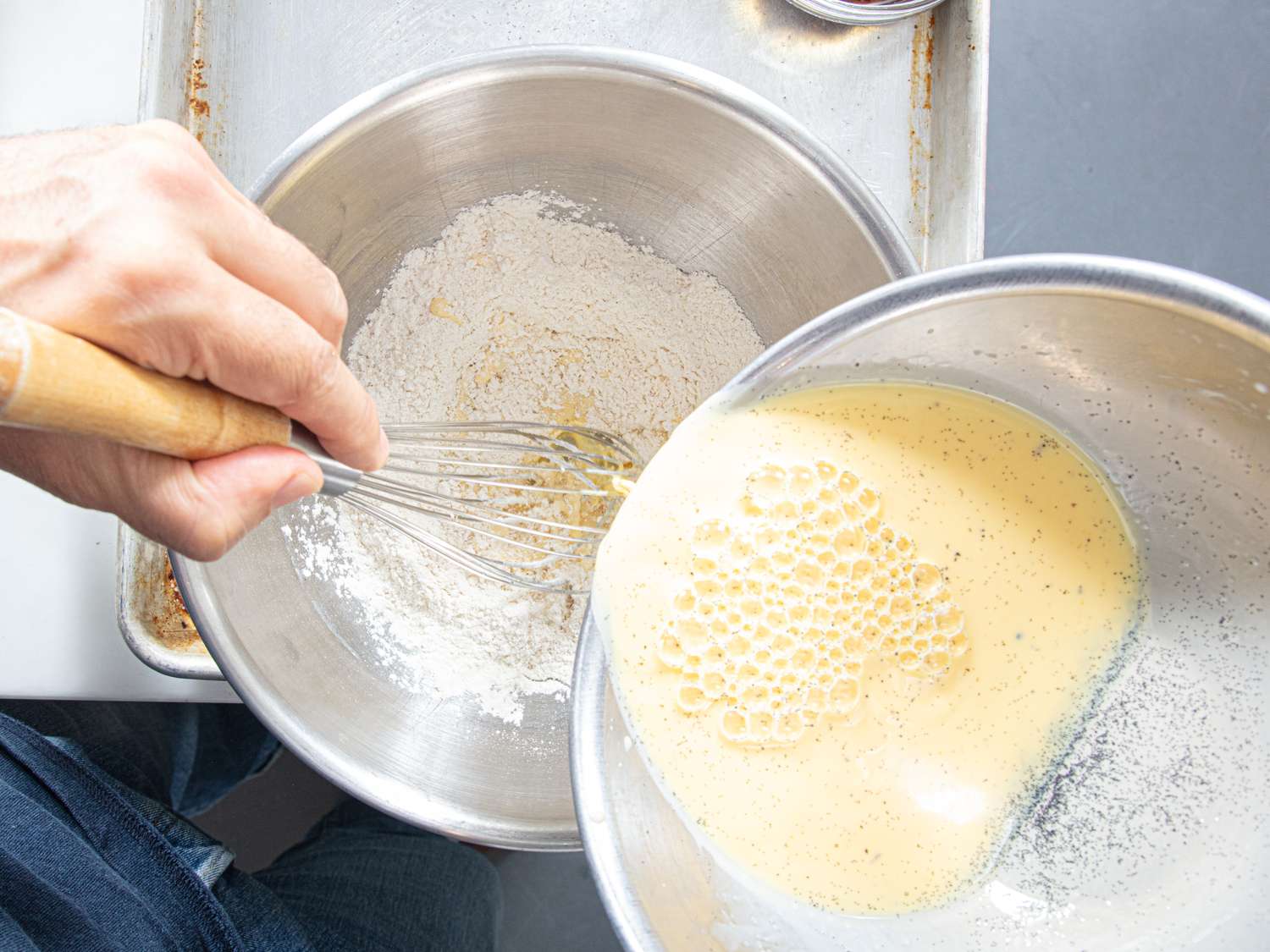Mixing batter in a bowl liquid mixture being poured into dry ingredients while whisking