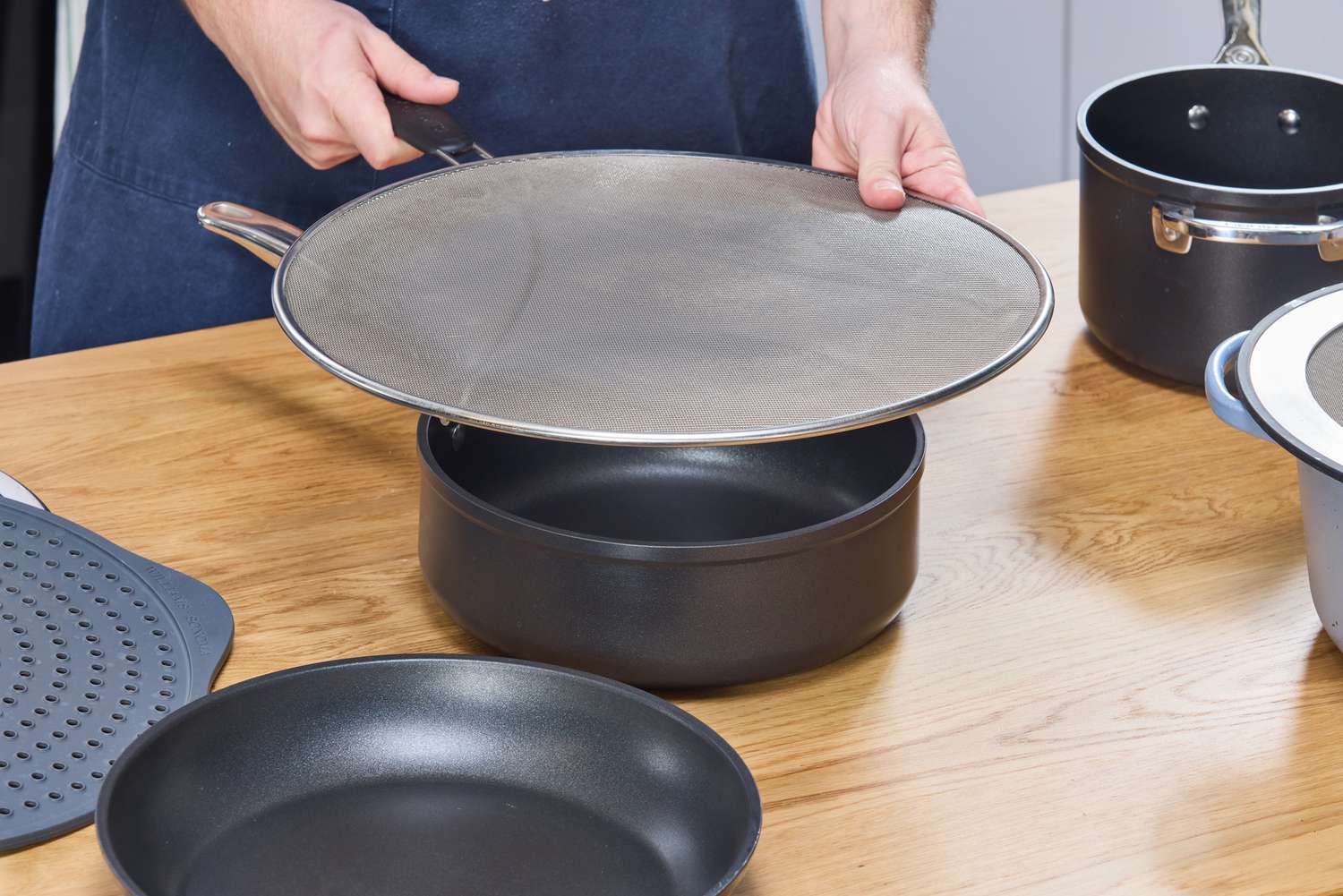 a person putting a splatter screen on a shallow pot