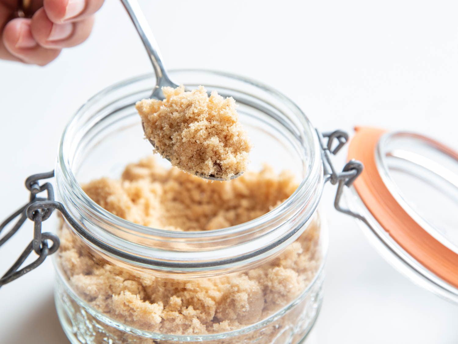 Taking a spoonful of brown sugar out of an airtight container with a rubber gasket lid.