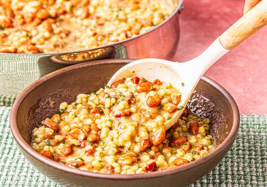 Bowl of barley and cranberry bean soup being served with a spoon dish in a rustic setting