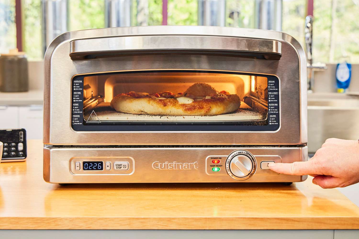 A person presses a button on the Cuisinart CPZ-120 Stainless Steel Indoor Pizza Oven
