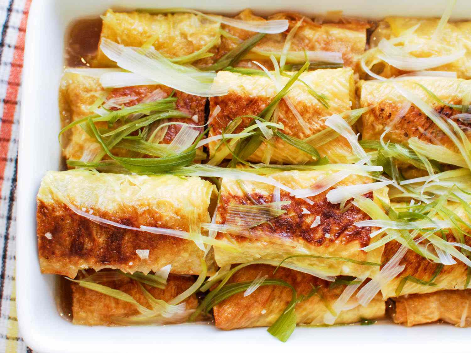A platter of stuffed bean curd rolls, garnished with sliced scallion.