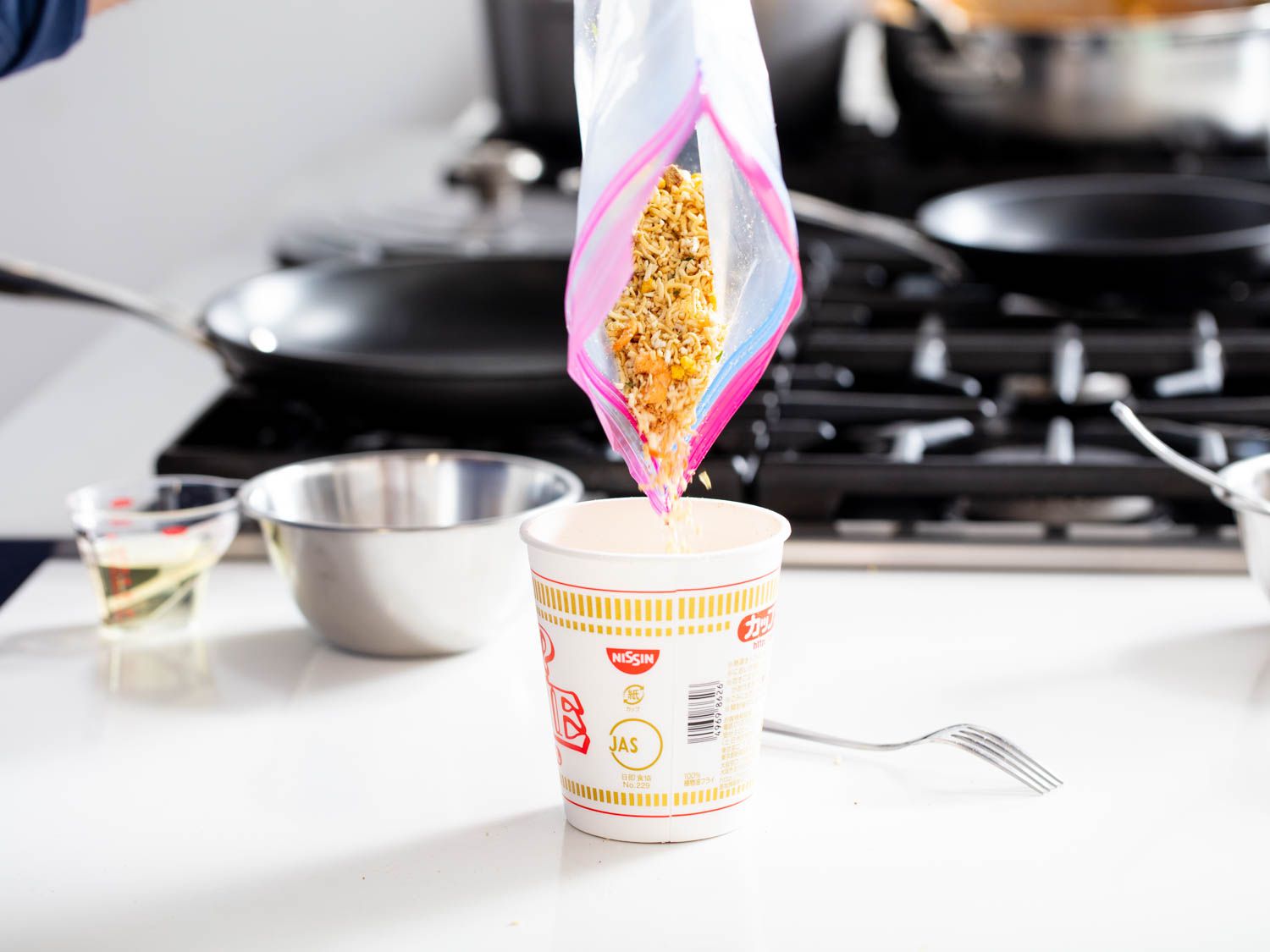 A ziplock containing the crushed noodles is emptied into their styrofoam cup.