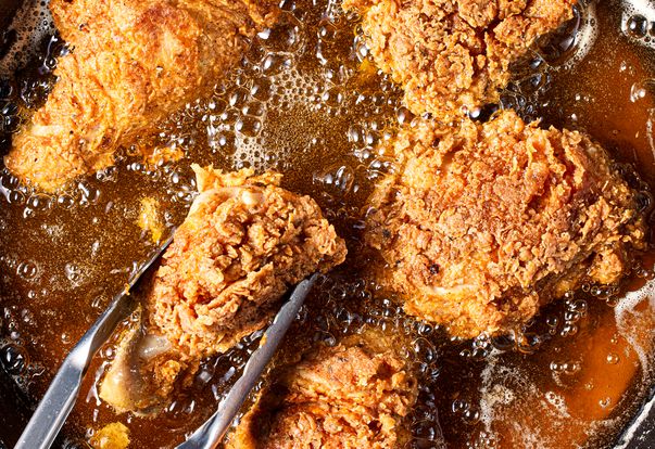 Closeup of fried chicken pieces being cooked in oil with tongs