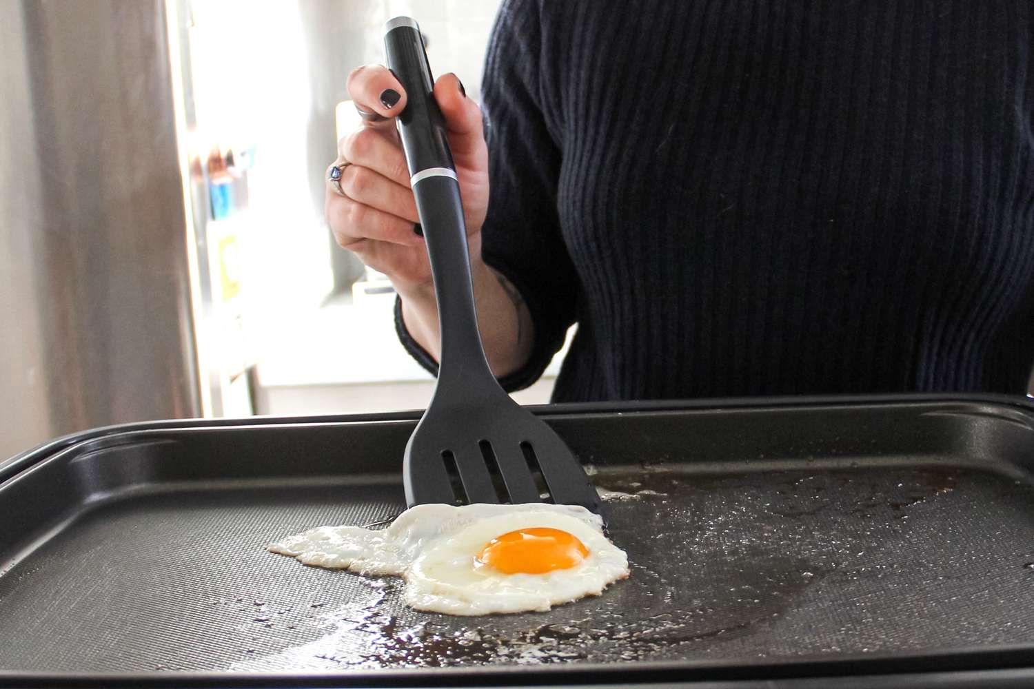 A person lifting a fried egg from a nonstick griddle with a food turner.
