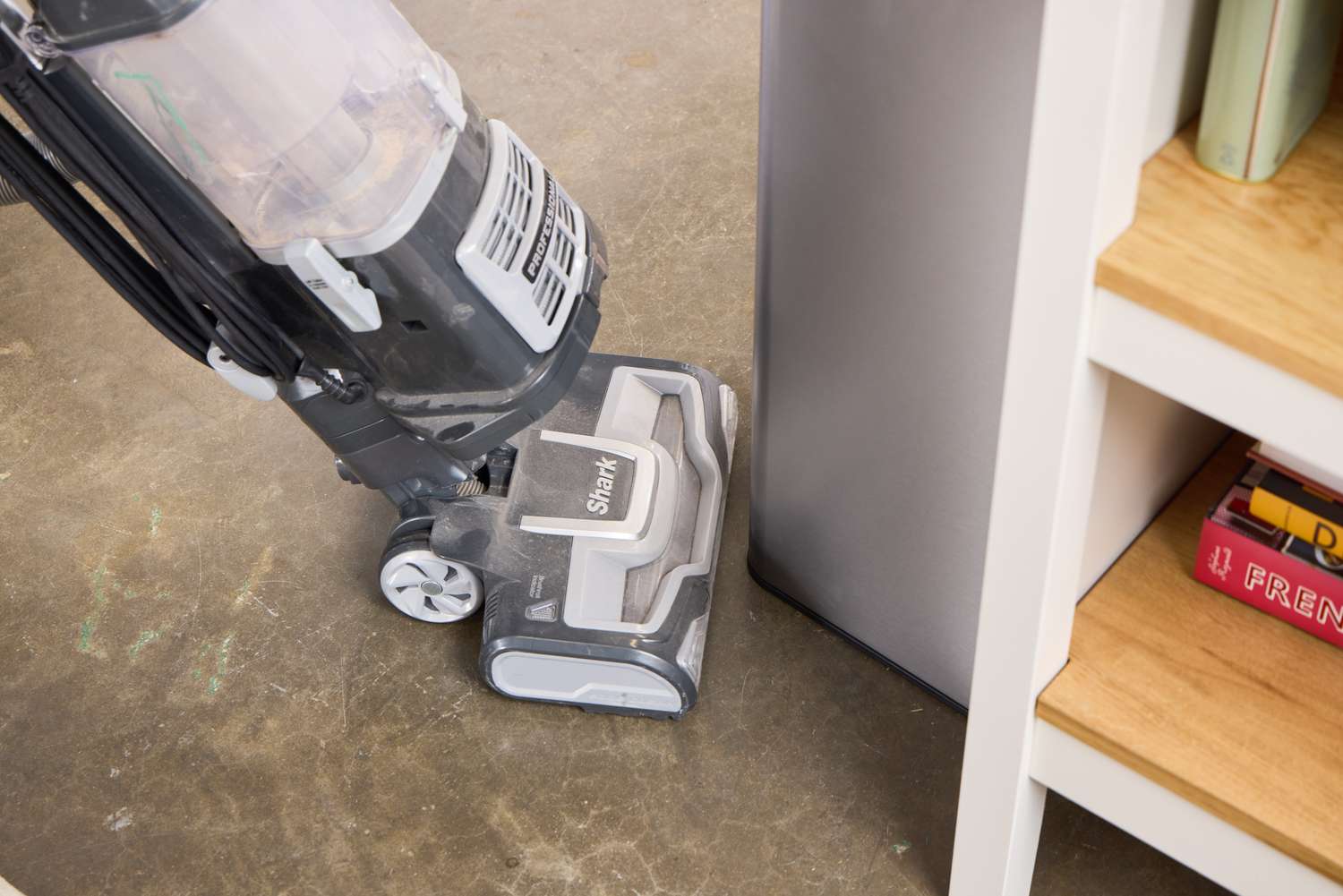 A person vacuums around the Kohler Stainless Steel 13-Gallon Step Trash Can
