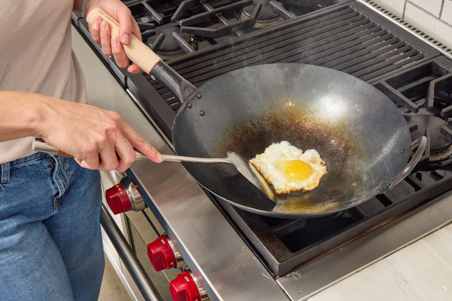 A person fries an egg in the Mammafong Pre-Seasoned Blue Carbon Steel Flat-Bottom Pow Wok