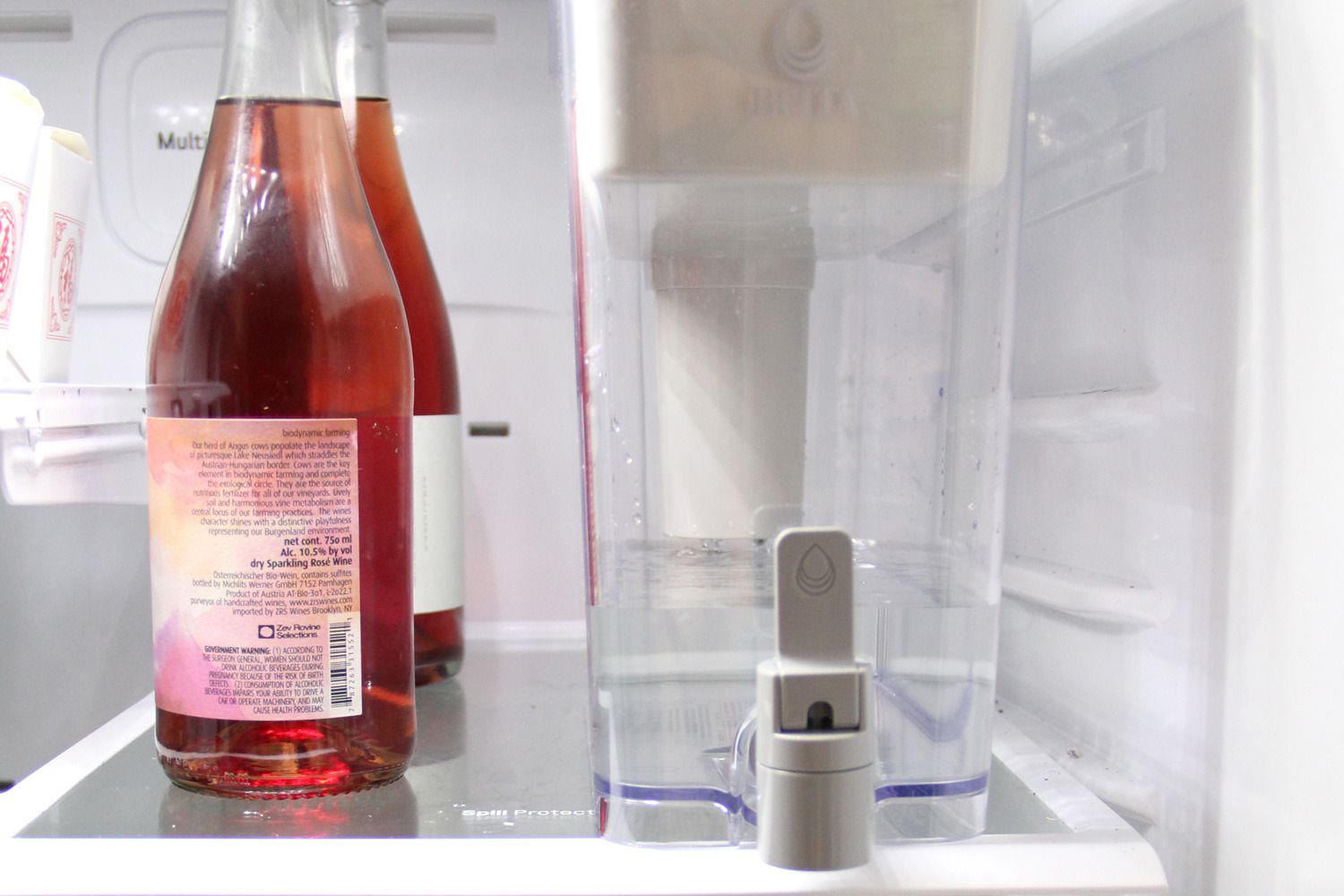 a water dispenser next to a few bottles of wine in the fridge