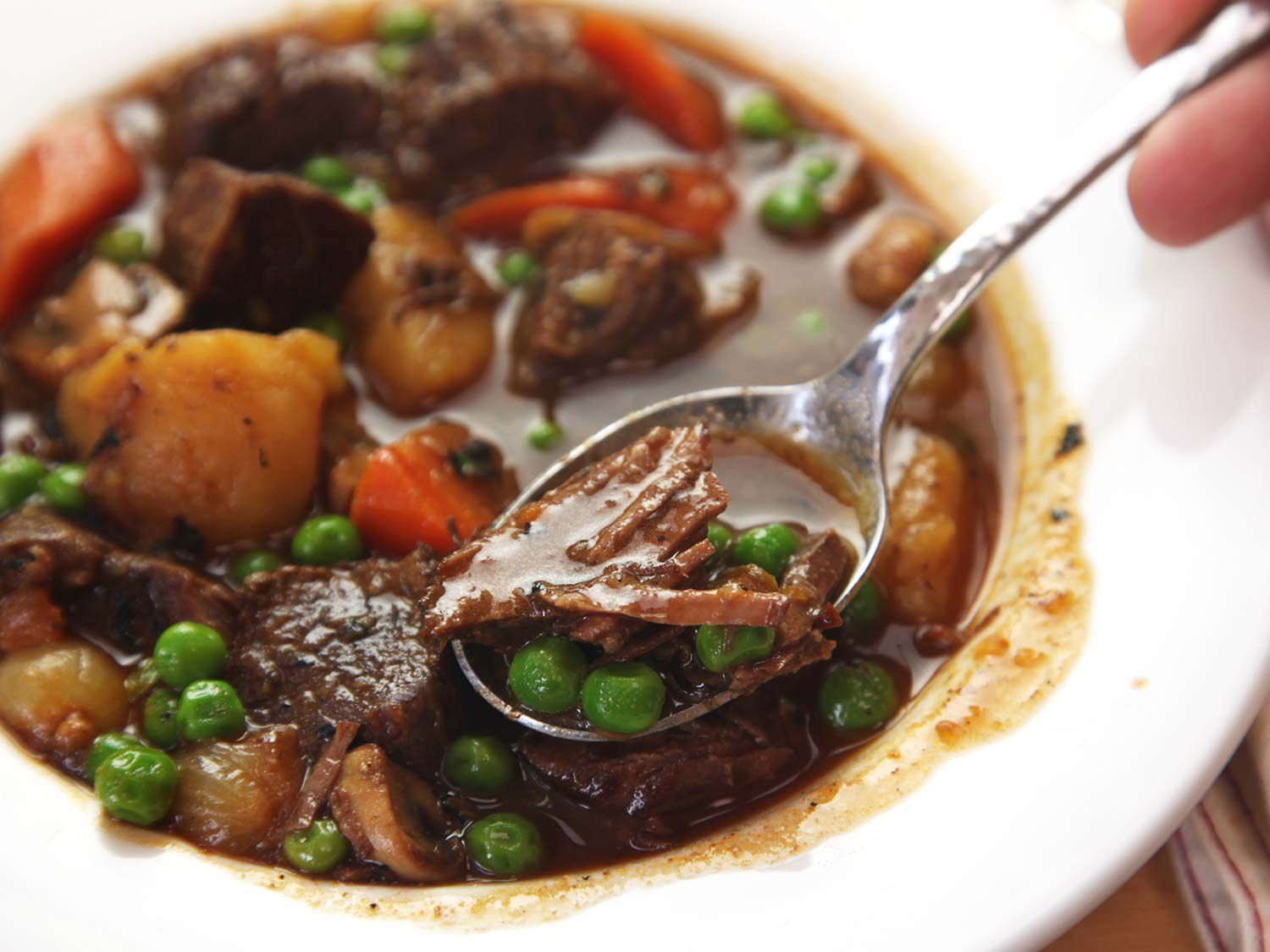 Spooning up beef and peas from a serving bowl of beef stew and vegetables. 