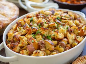 A dish of stuffing with herbs and bread cubes on a table with other dishes