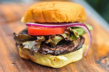 Side view of a Balsamic Marinated Portobello Burger, served in a bun with lettuce, tomato, and red onion.