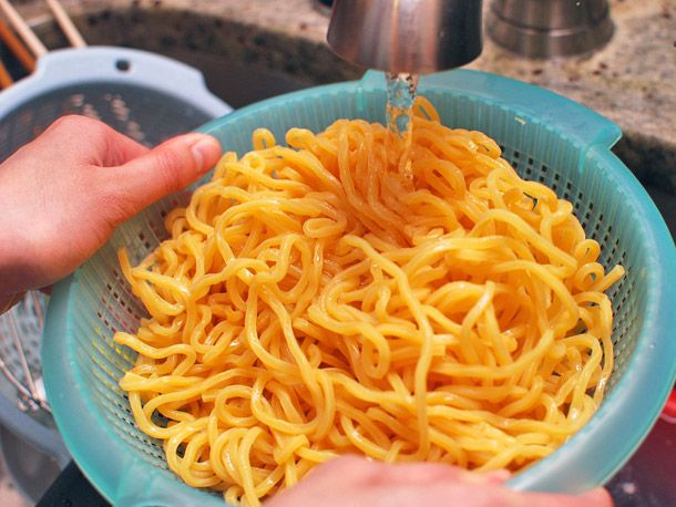 Lo Mein Noodles in a strainer being washed with water