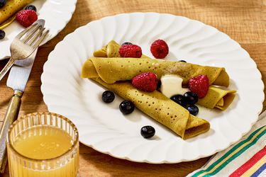 ployes with butter and berries on white dishes, with a fork and knife, striped napkin, and a wooden tabletop