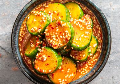 A bowl of marinated cucumber slices topped with sesame seeds and red chili flakes