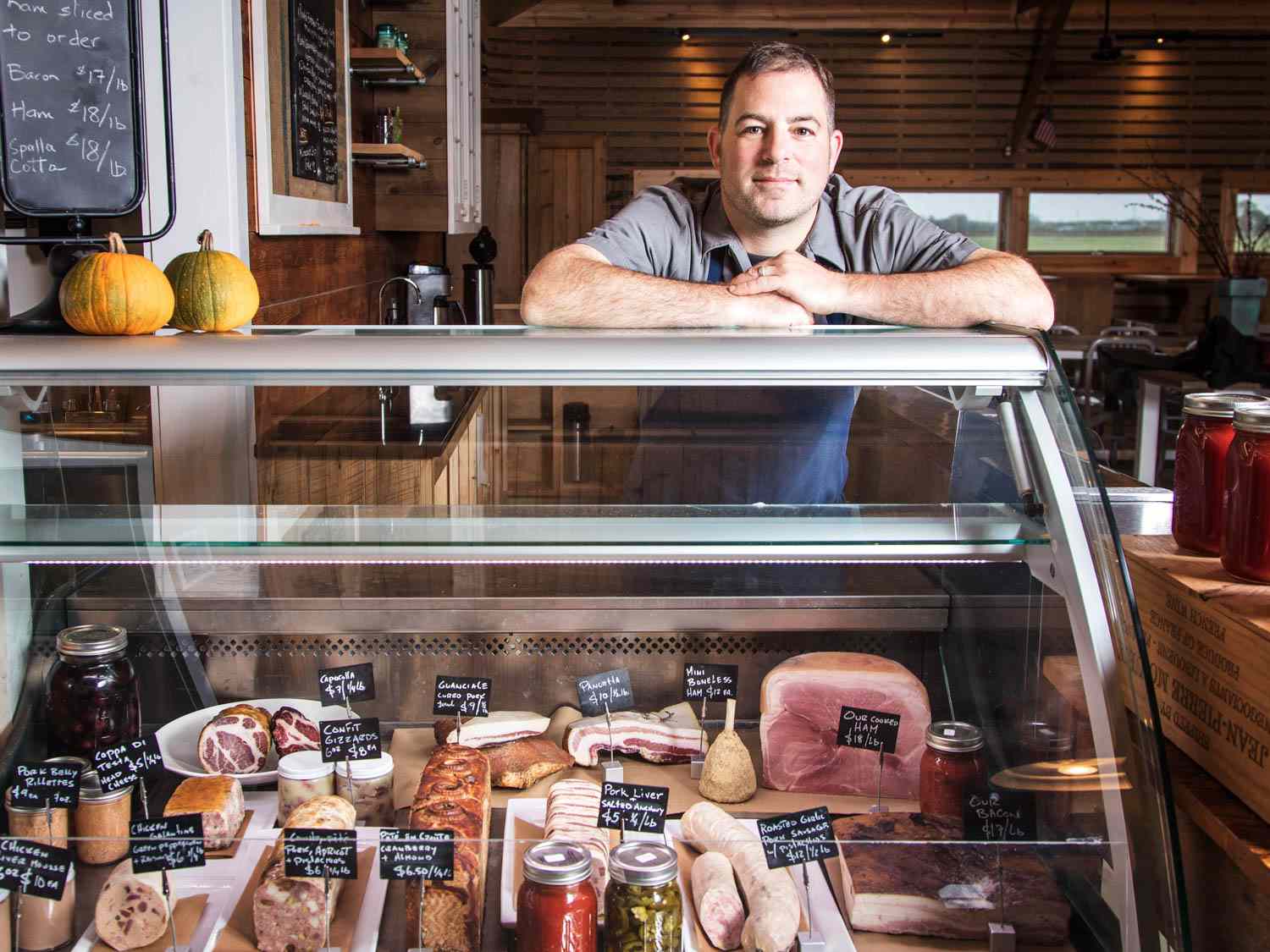 Julien Shapiro leans on a cold case filled with assorted charcuterie and pâtés at 8 Hands Farm in Cutchogue, NY.