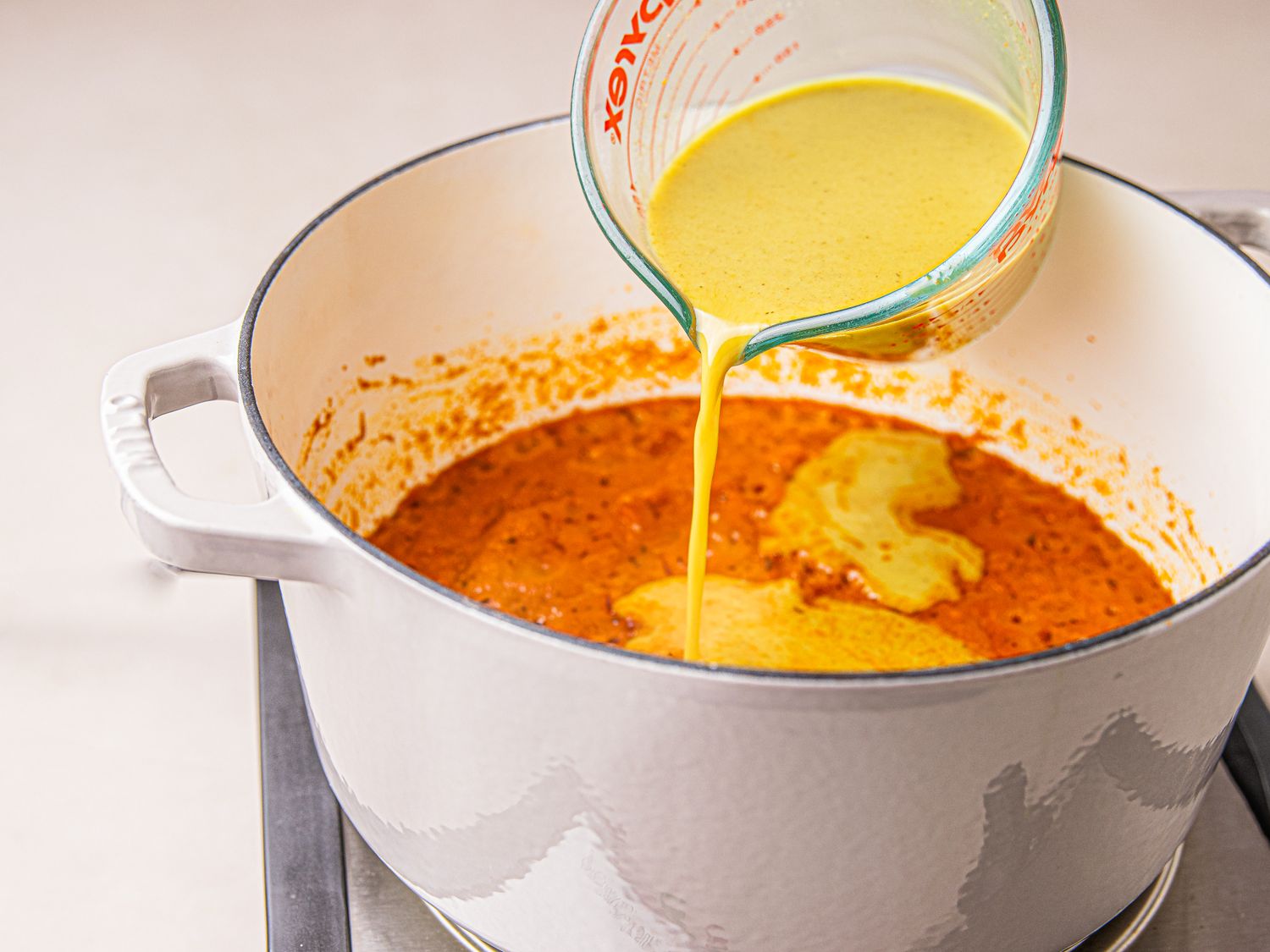 Liquid being poured from a measuring cup into a pot of stew underway on a stovetop
