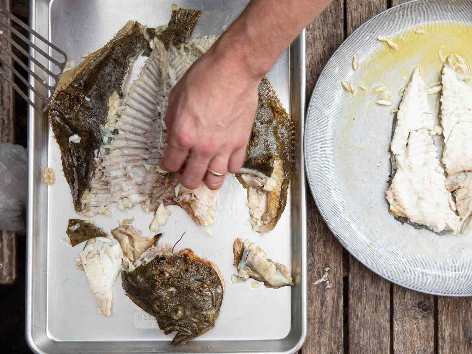 Portioning and deboning the turbot on a rimmed baking sheet after it comes off the grill.