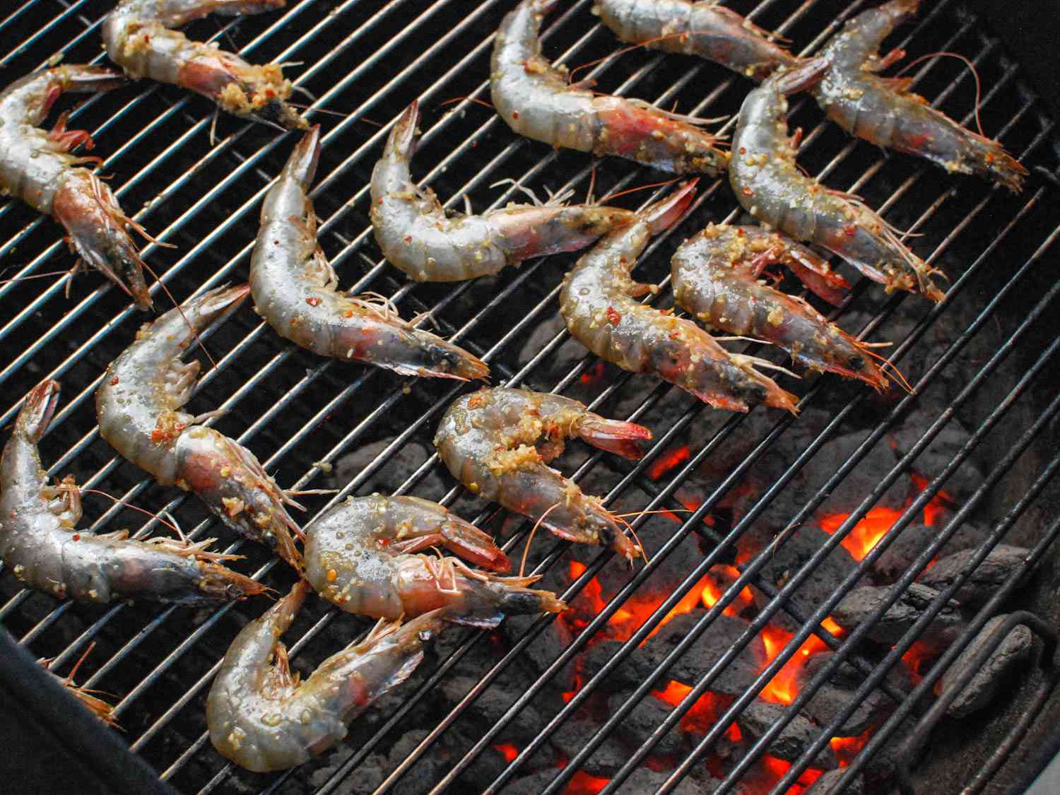 The marinated shrimp are arranged on the grill grate directly above glowing coals.