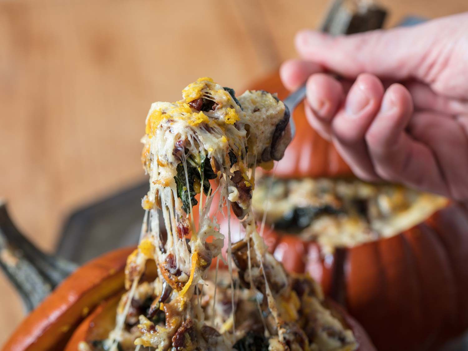 Stuffed pumpkins with Gruyere, mushrooms, kale (for Thanksgiving and holidays), fork pulling a bite with stretchy melted cheese.