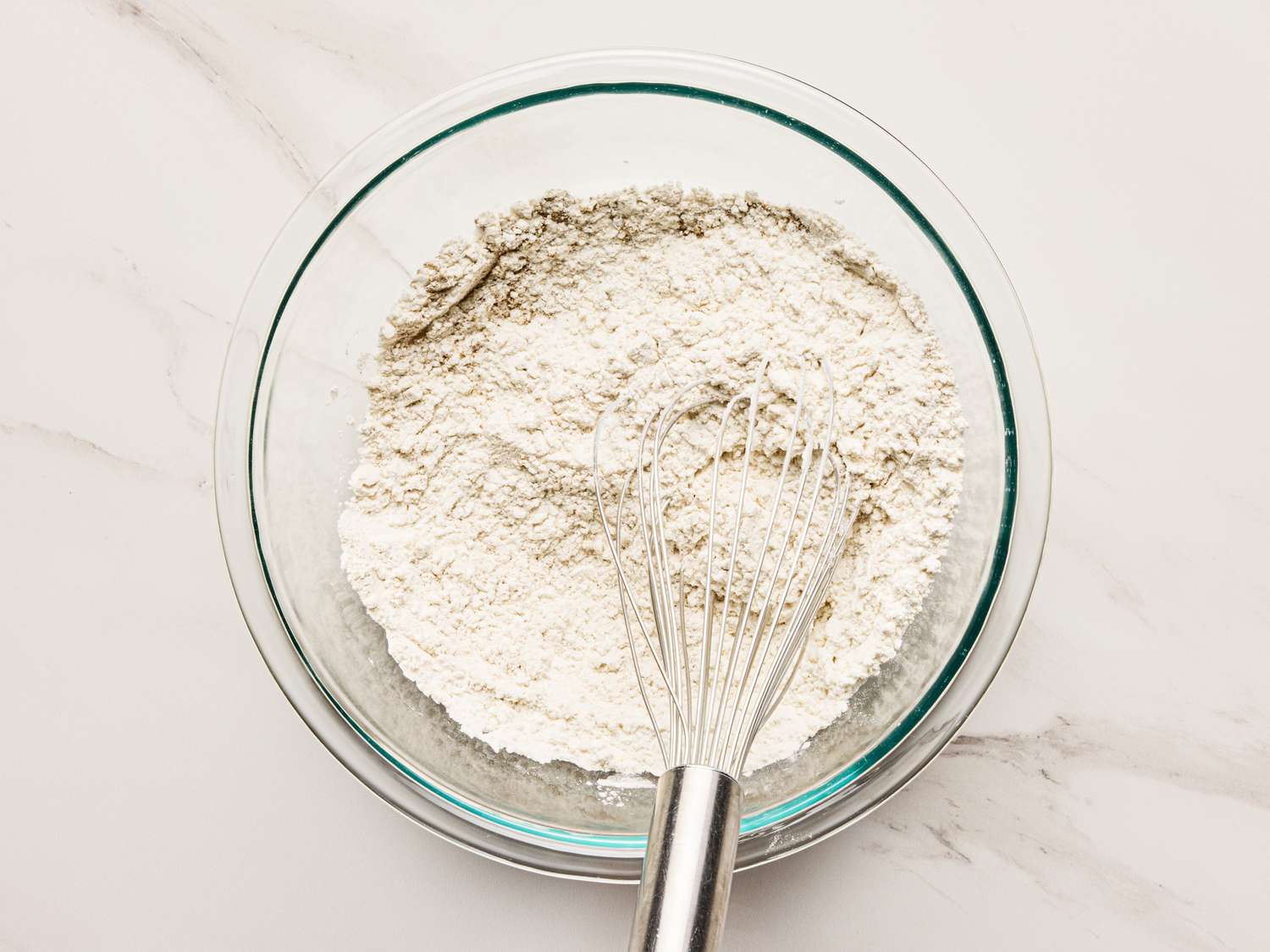 A mixing bowl containing flour with a whisk placed inside