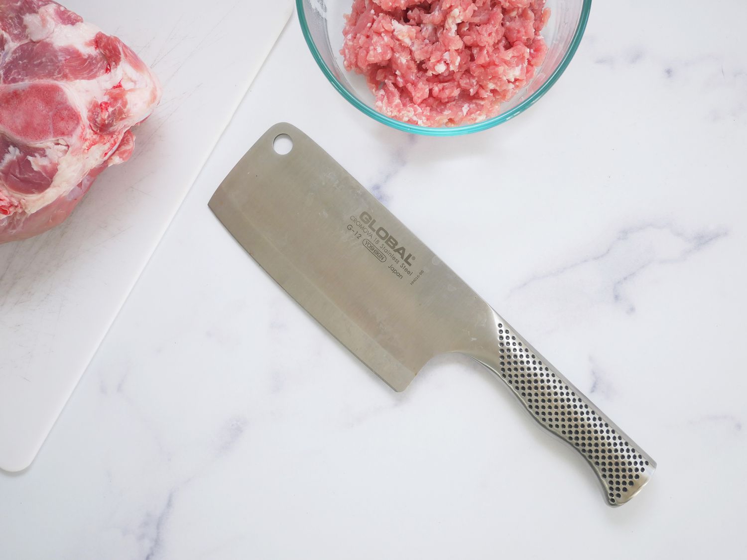 Global 6.5-Inch Meat Cleaver on a marble counter with a bowl of minced pork shoulder and the pork shoulder on a cutting board