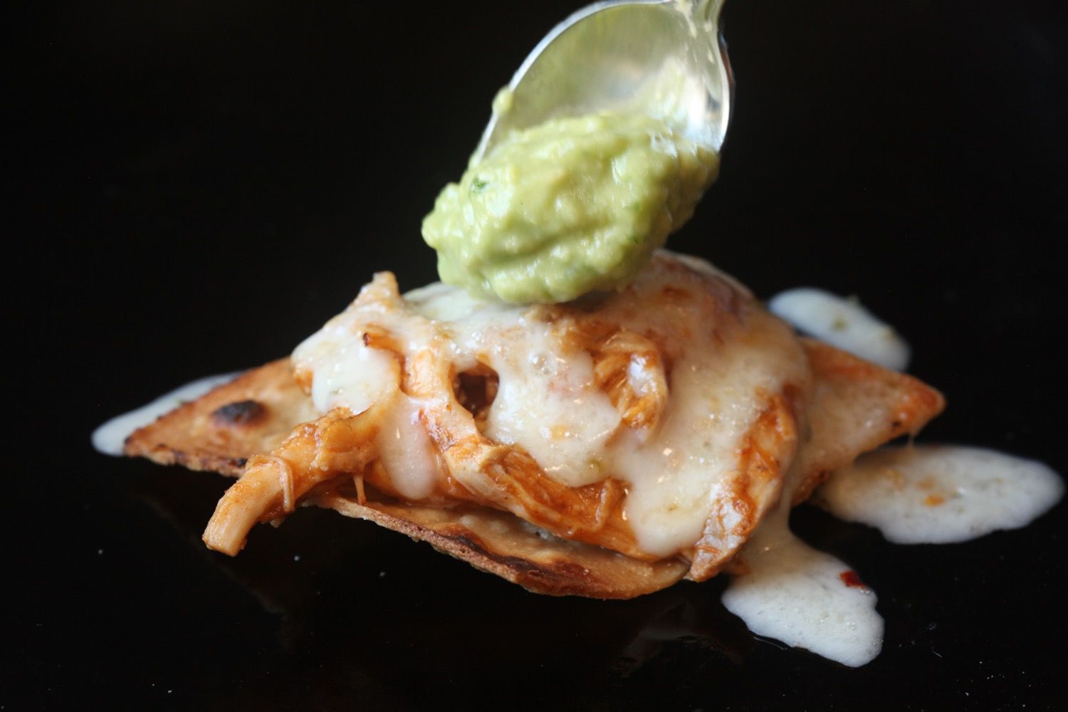 Spooning some guacamole over a nacho made with chicken tinga and cheese. 