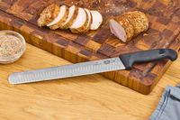 The Victorinox Fibrox Pro 12-Inch Slicing Knife with Granton Blade rests on a cutting board