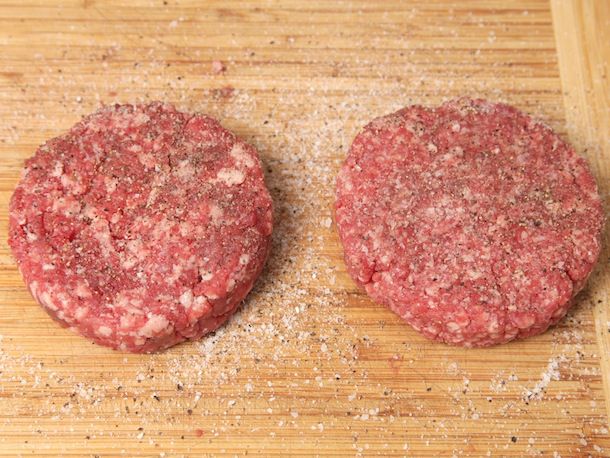A coarsely ground and finely ground beef patty, raw and liberally seasoned with salt and pepper.