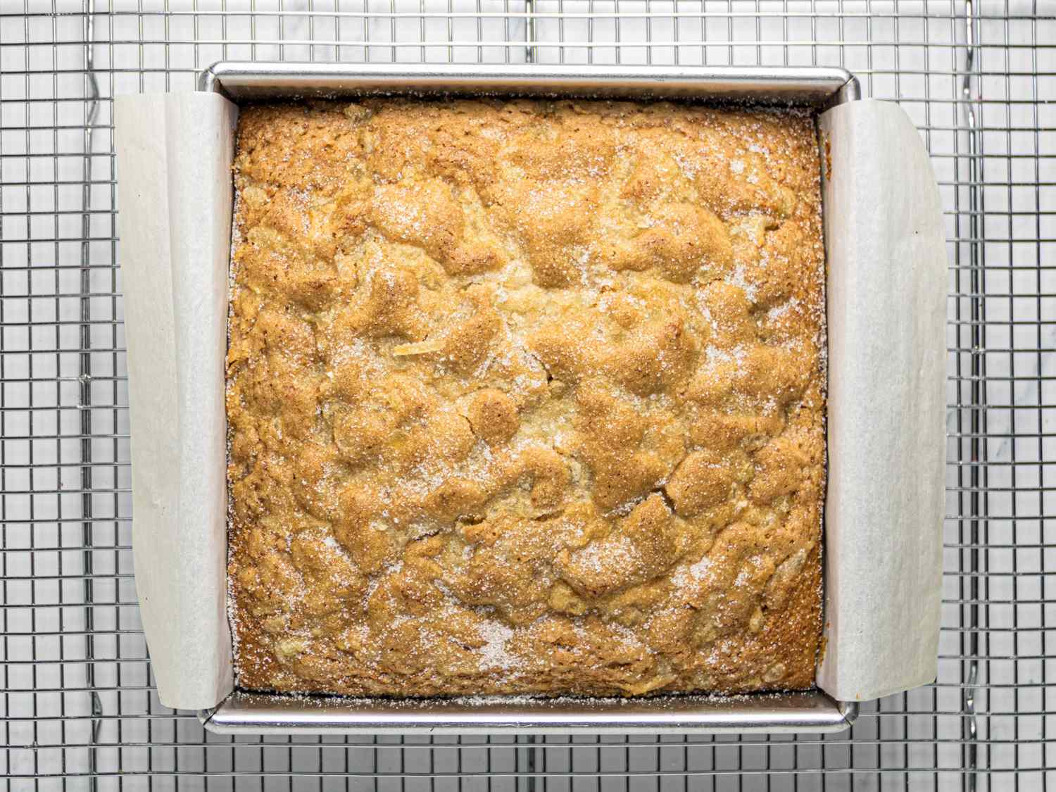 Baked applesauce snack cake in a square pan on a cooling rack