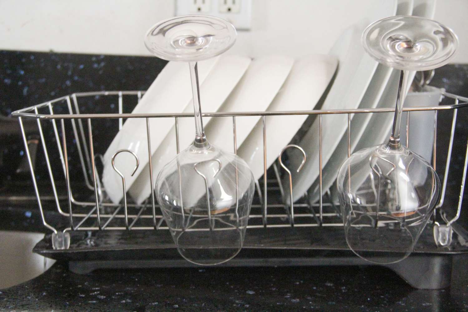 a dish rack with plates and bowls and two wine glasses on it draining water