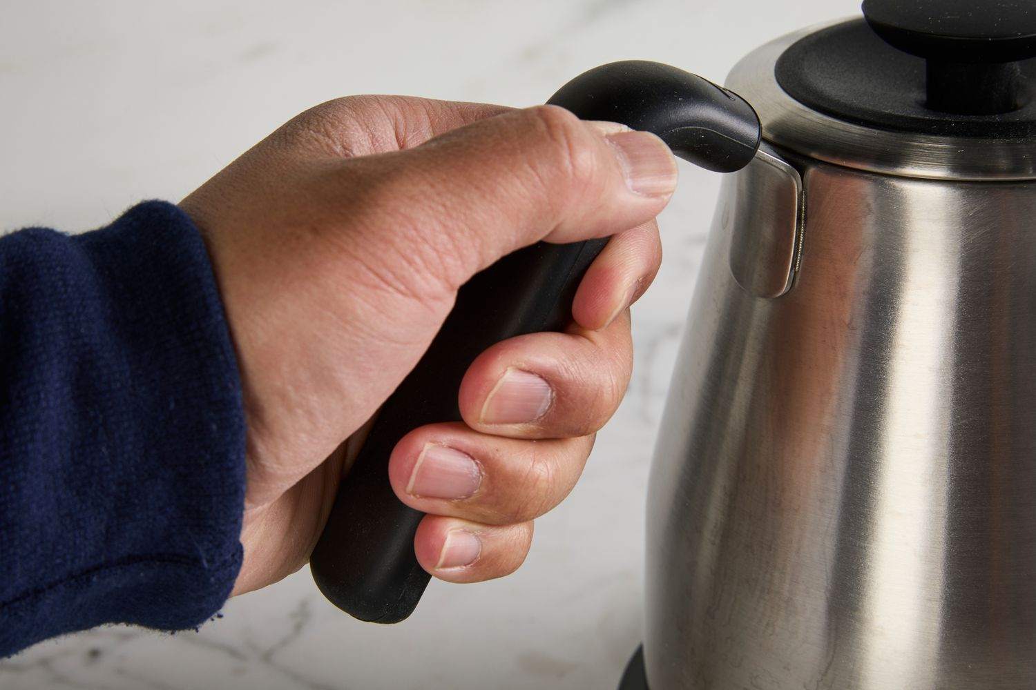 A person gripping the handle of the OXO gooseneck kettle.