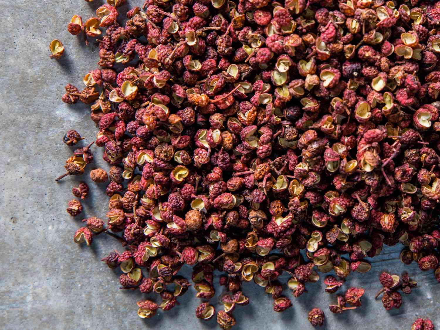A pile of rose-colored Sichuan peppercorns against grey backgroubnd