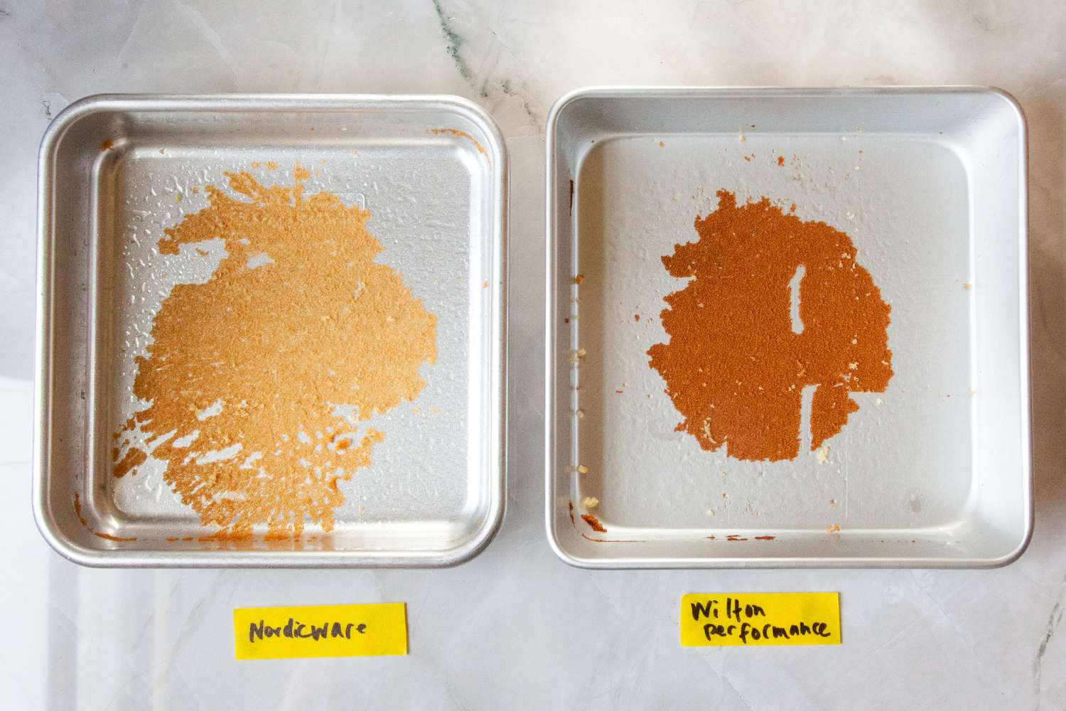 Two square baking pans compared for performance with residue on the bottom labeled Nordic Ware and Wilton Performance
