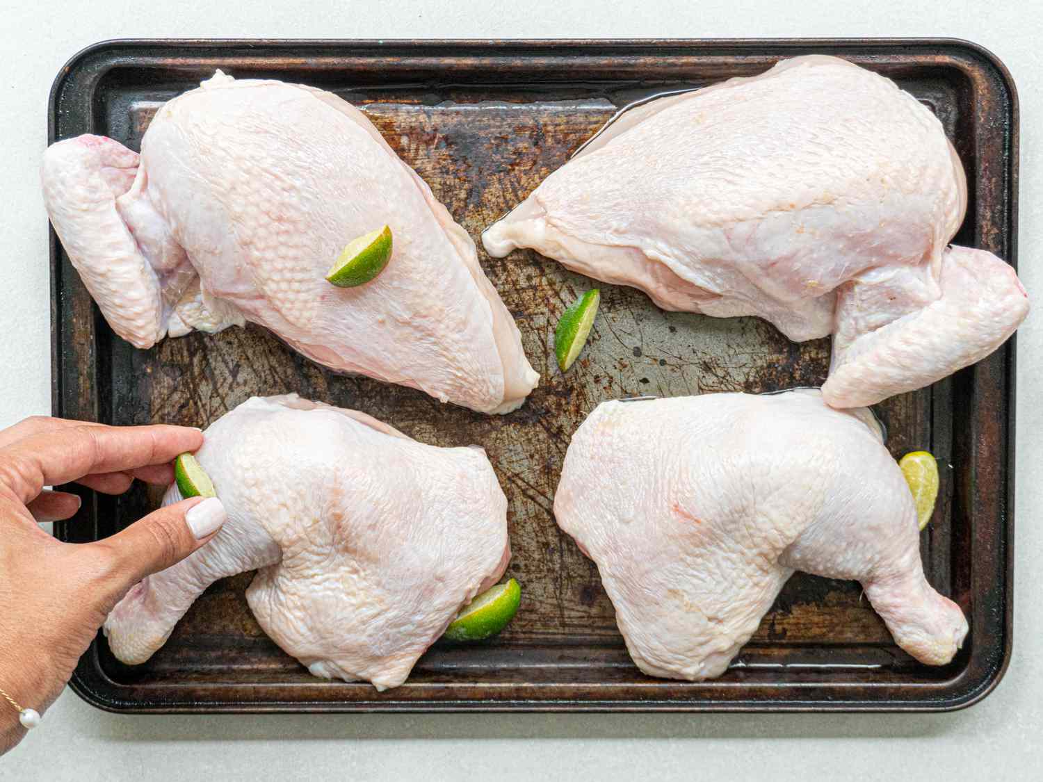 Divided chicken being rubbed with lime on a sheet pan.