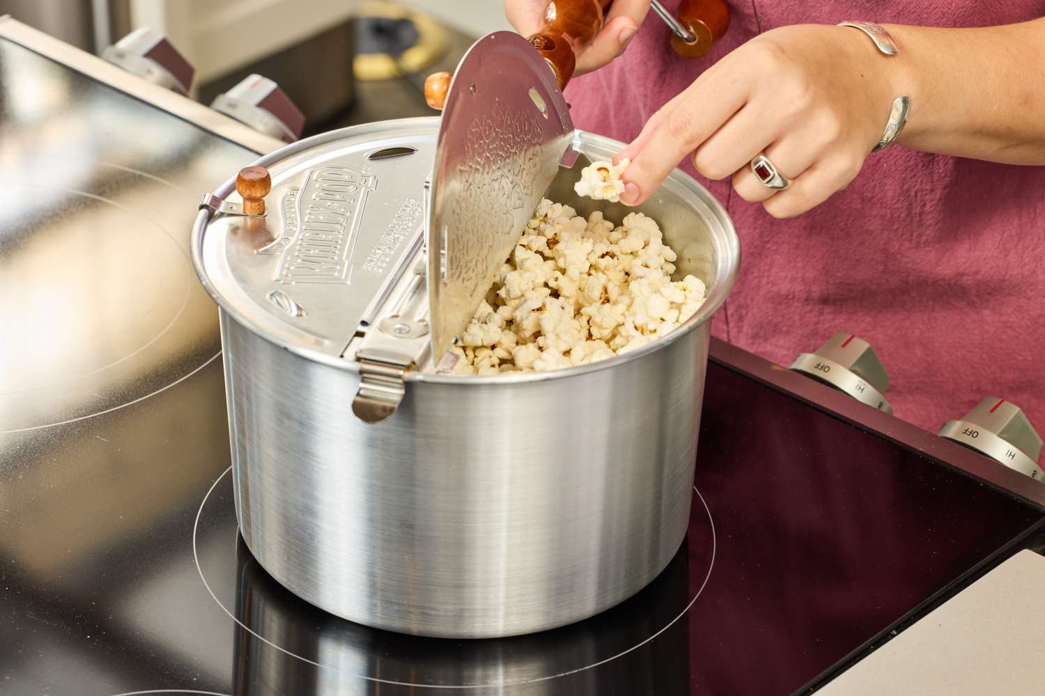 A person removes popcorn from the Wabash Valley Farms Original Whirley-Pop Popcorn Popper Stainless Steel after popping