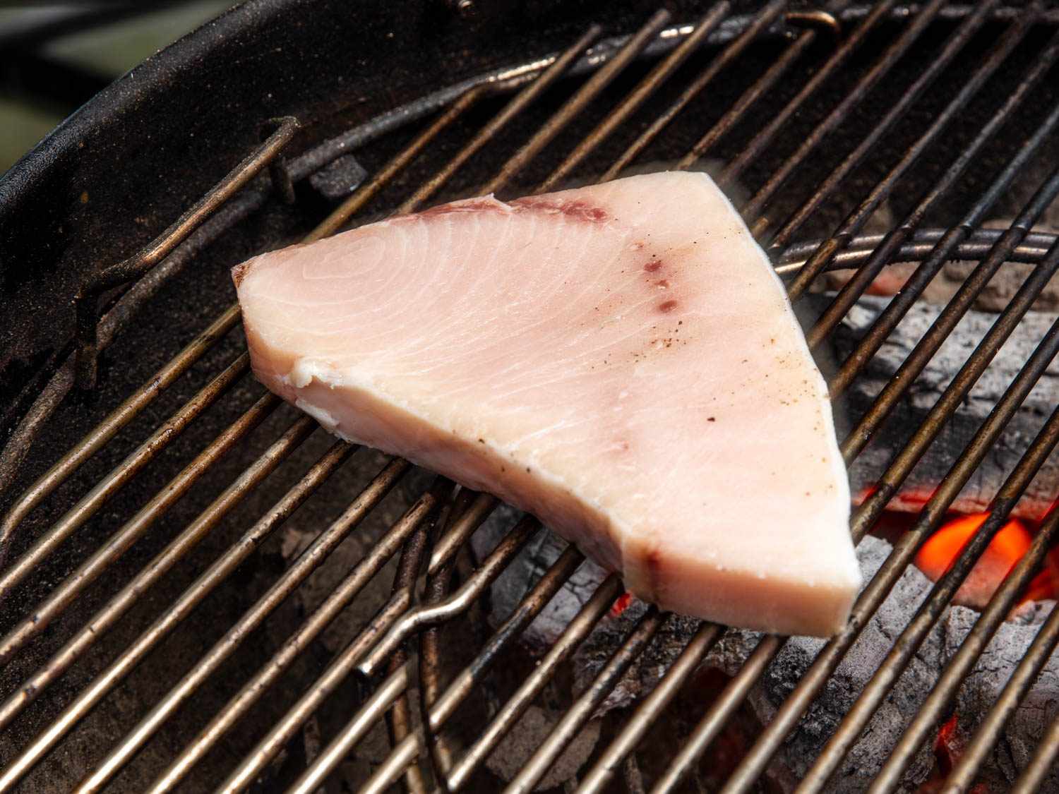 A piece of mostly raw swordfish steak on the grill.