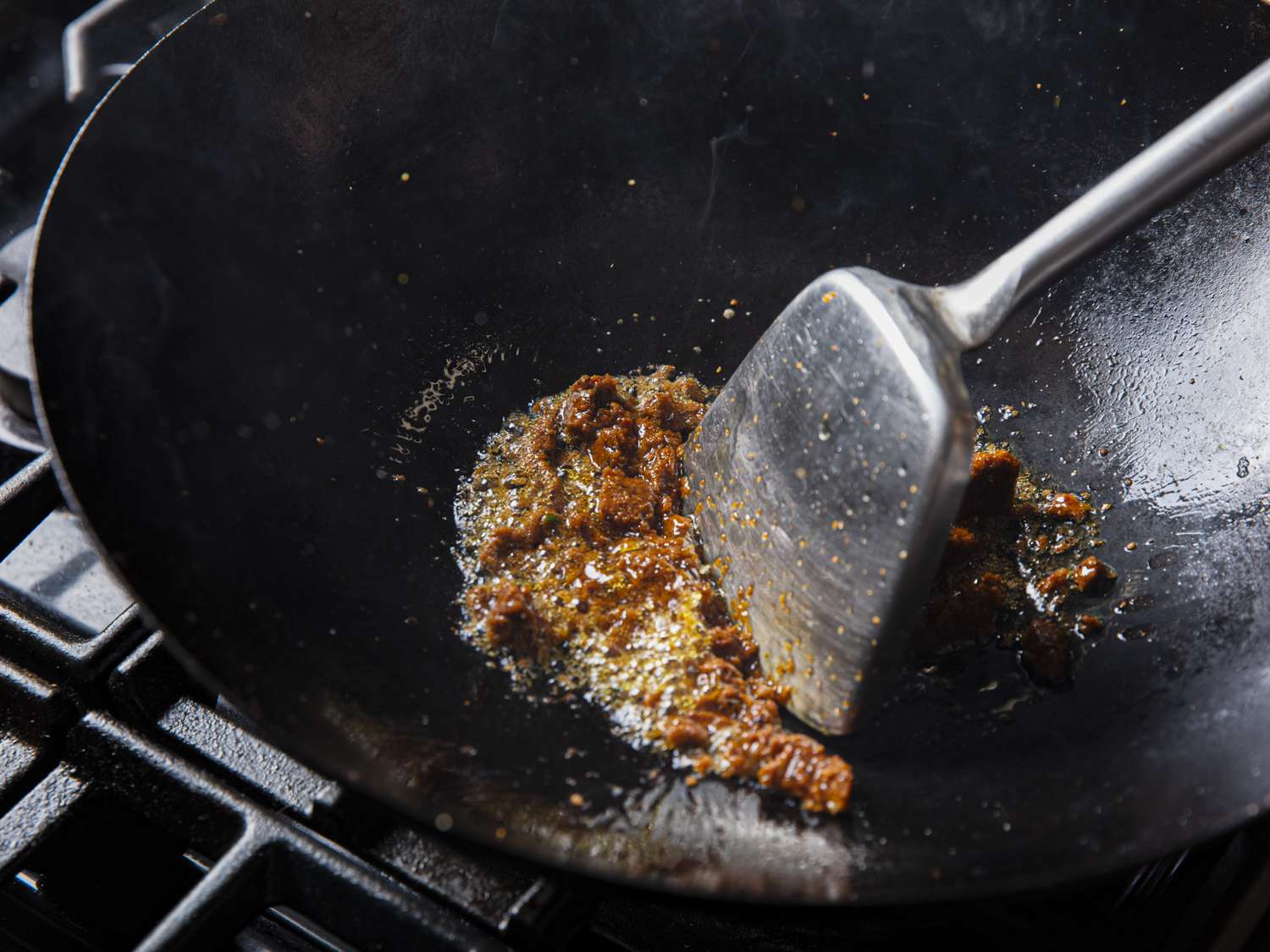 A metal spatula pushing curry around in oil in a wok