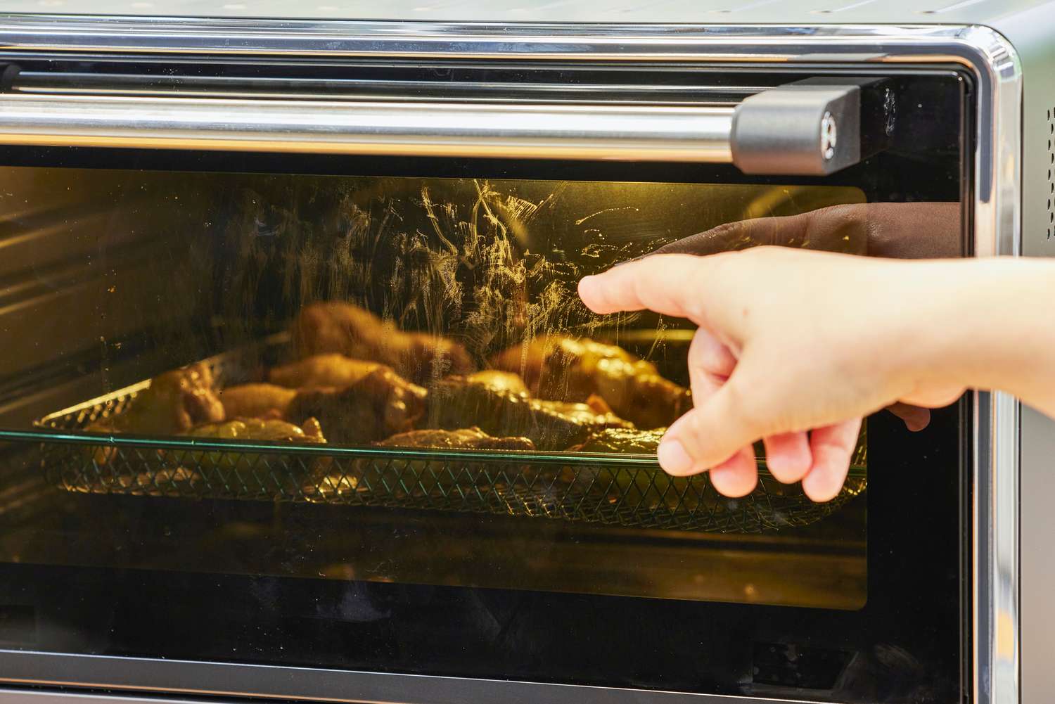 A hand pointing to chicken cooking in the KitchenAid Dual Convection Countertop Oven with Air Fryer