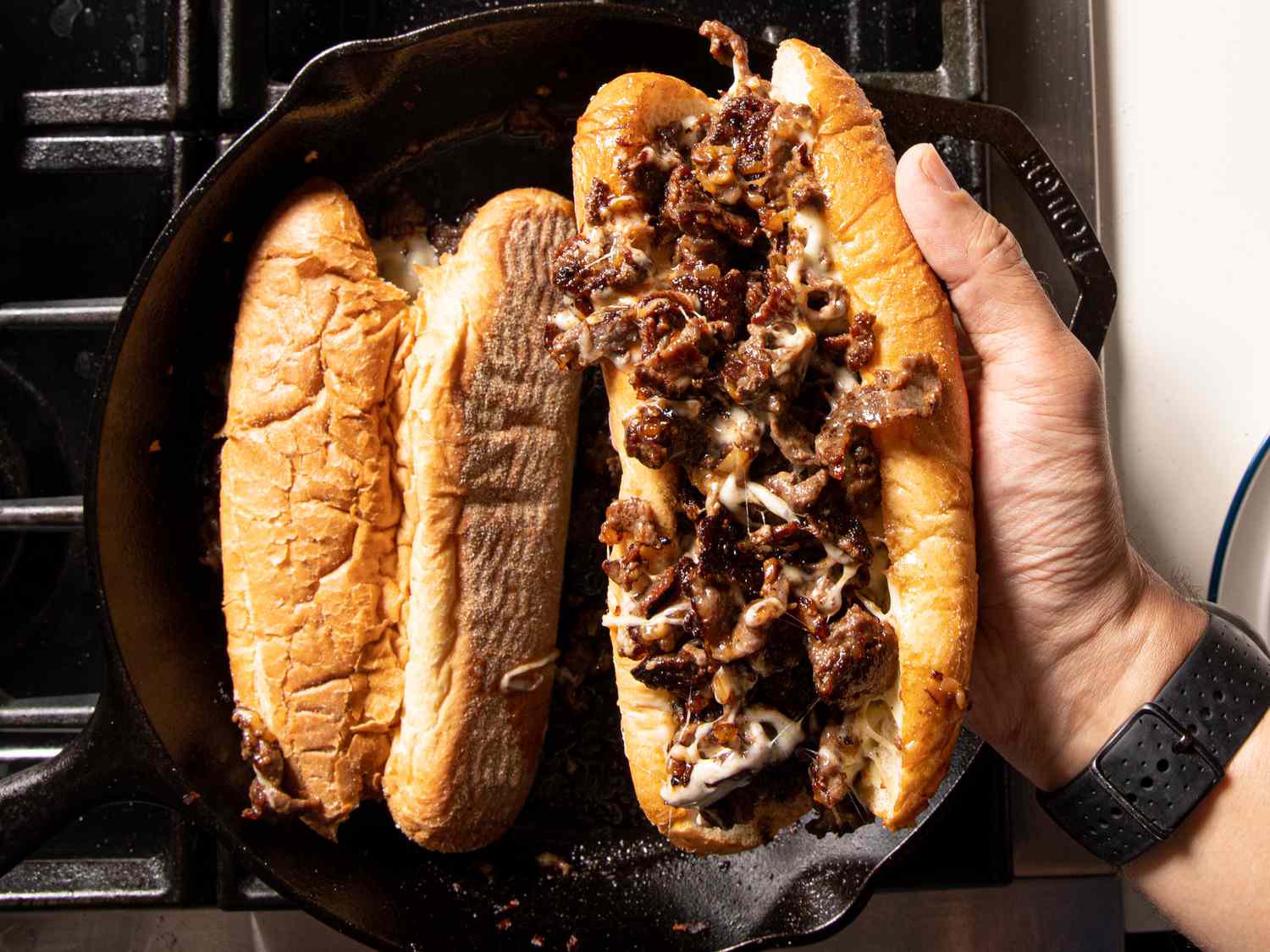 Philly cheesesteak in hand over skillet