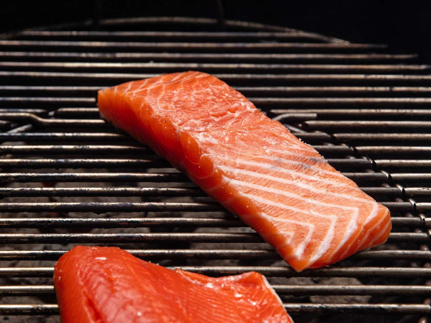 A piece of salmon, still mostly raw, skin side down on the grill.