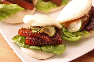 Several pork belly buns with lettuce on a white platter, topped with quick pickles.