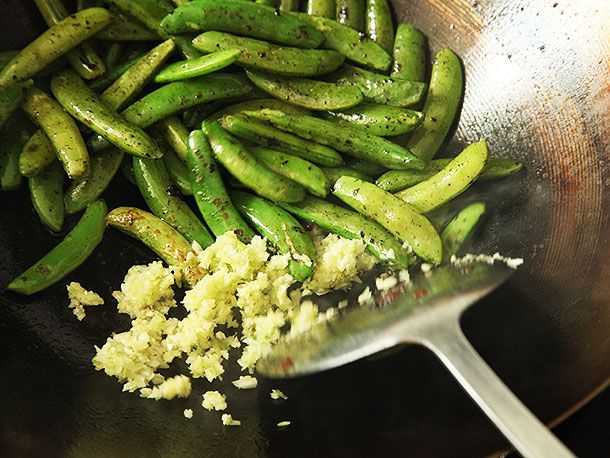 Wok-seared snow peas and ginger in a wok.