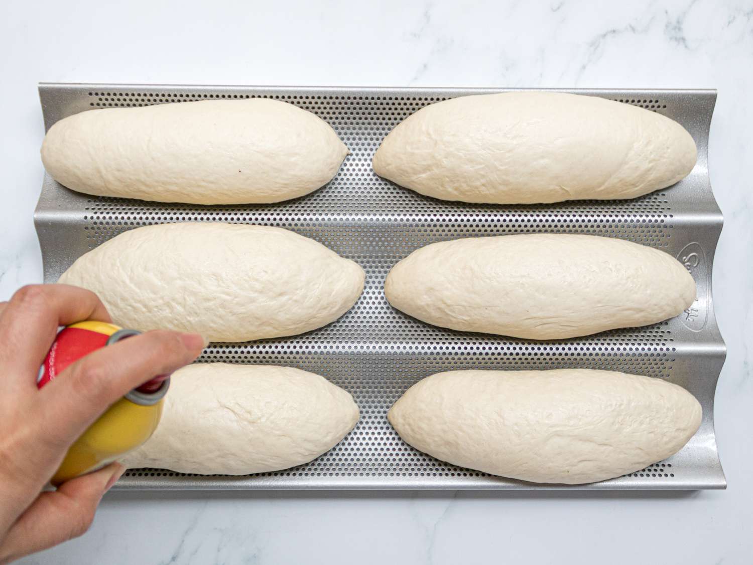 Overhead view of spraying banh mi loaves with cooking spray