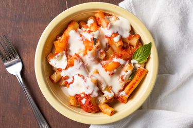 Overhead shot of bowl of baked ziti drizzled with Parmesan cream 