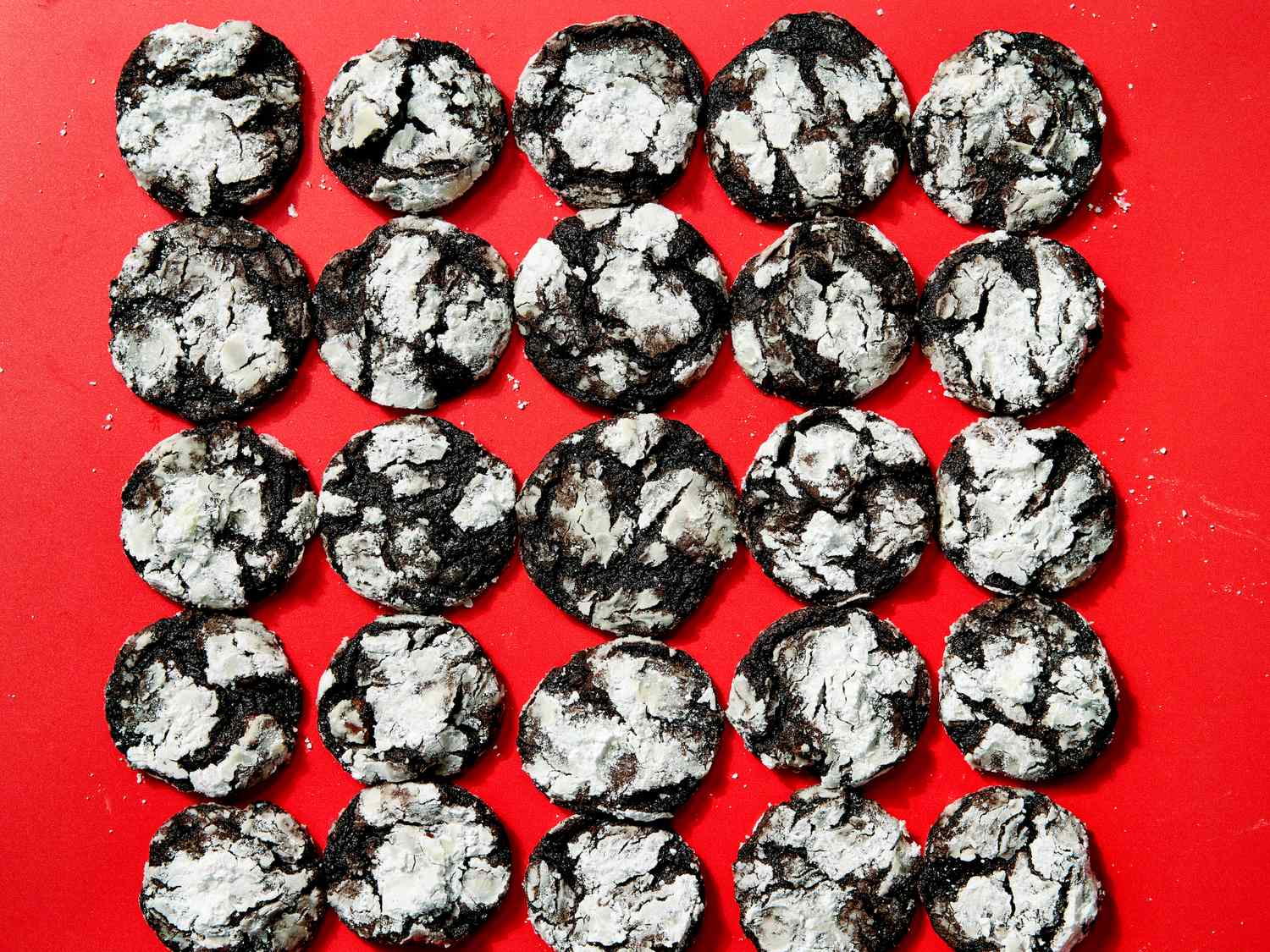 Rows of chocolate crinkle cookies on a red surface arranged neatly in a grid