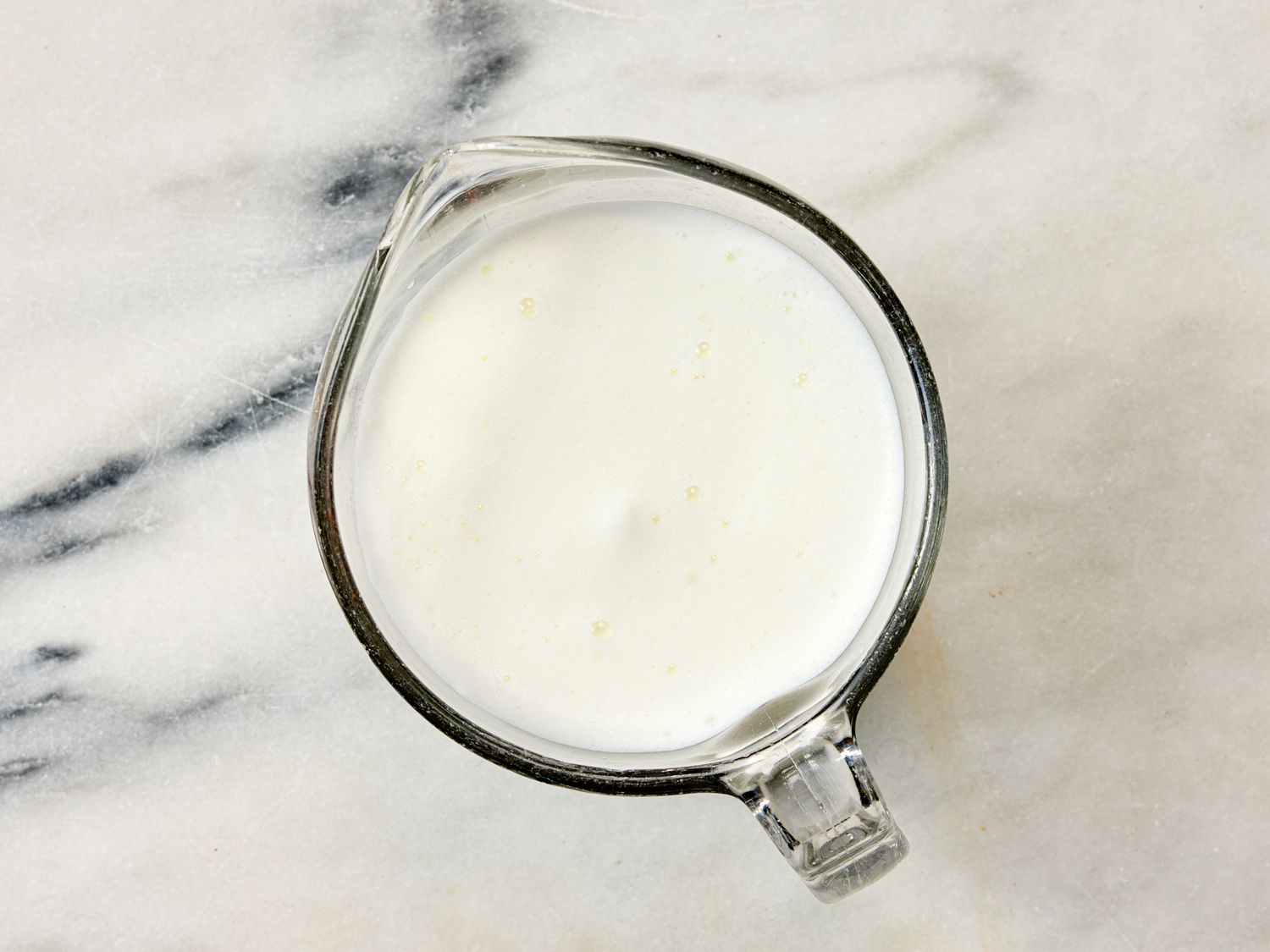 A glass measuring cup containing a white liquid sitting on a marble surface