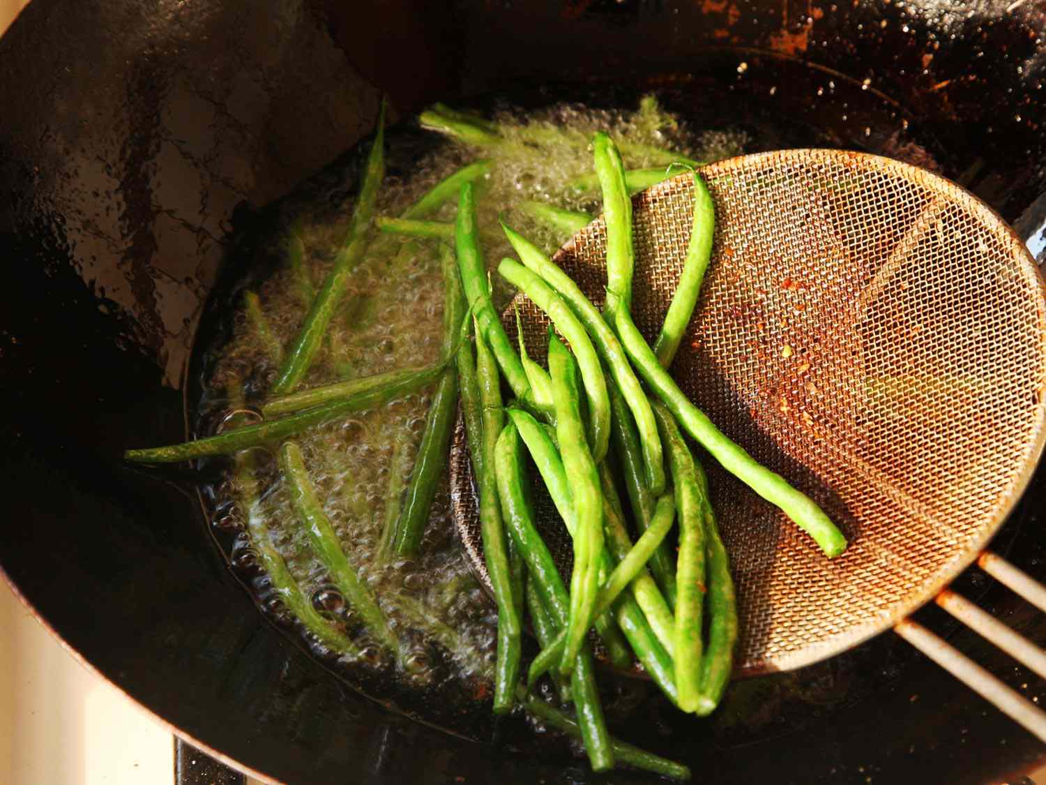 Green beans are added to a hot wok for the initial stage of the dry-frying process.