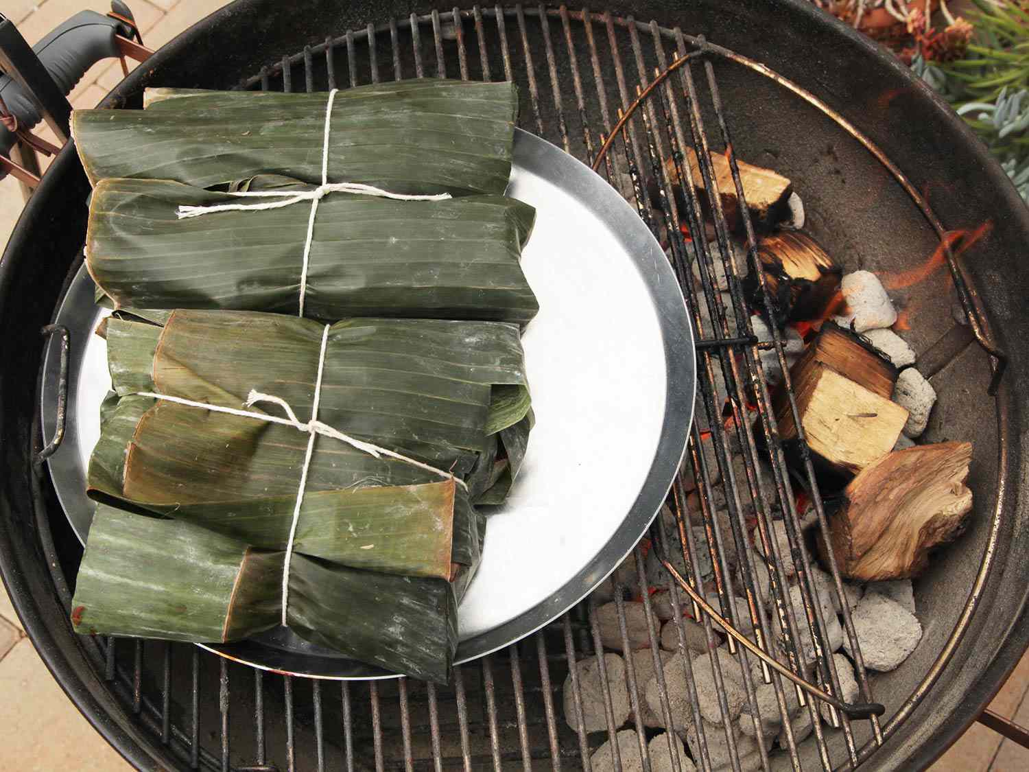 Roasting banana leaf-wrapped pork on a grill over indirect heat. 